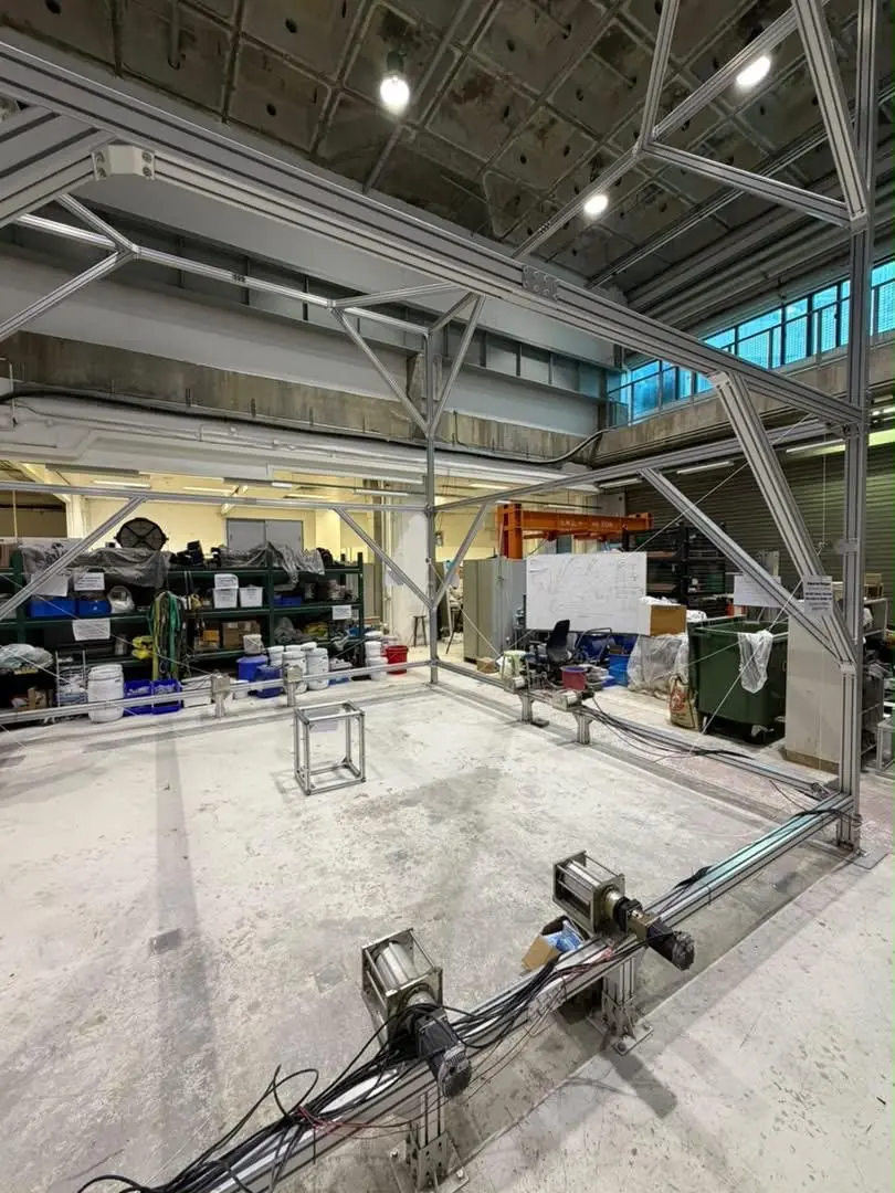 Another laboratory view of the CDPR showing the foreground winches, cable routing, and central metal carrier